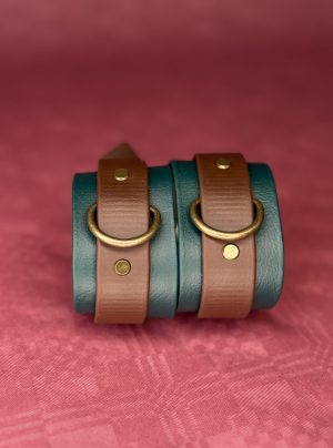 Grün-braune Biothane Cuffs vor rotem Hintergrund, stehend nebeneinander